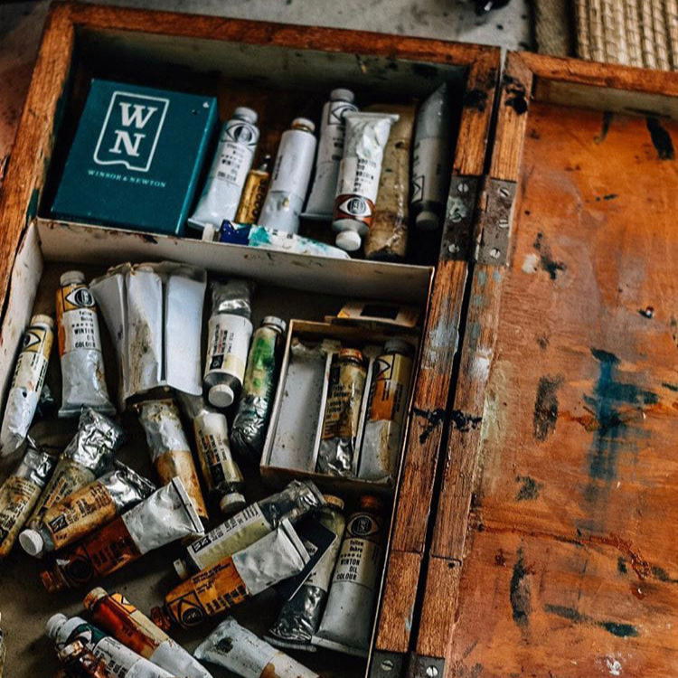 Old wooden box filled with art supplies including paint tubes and a box labeled 'WN'.
