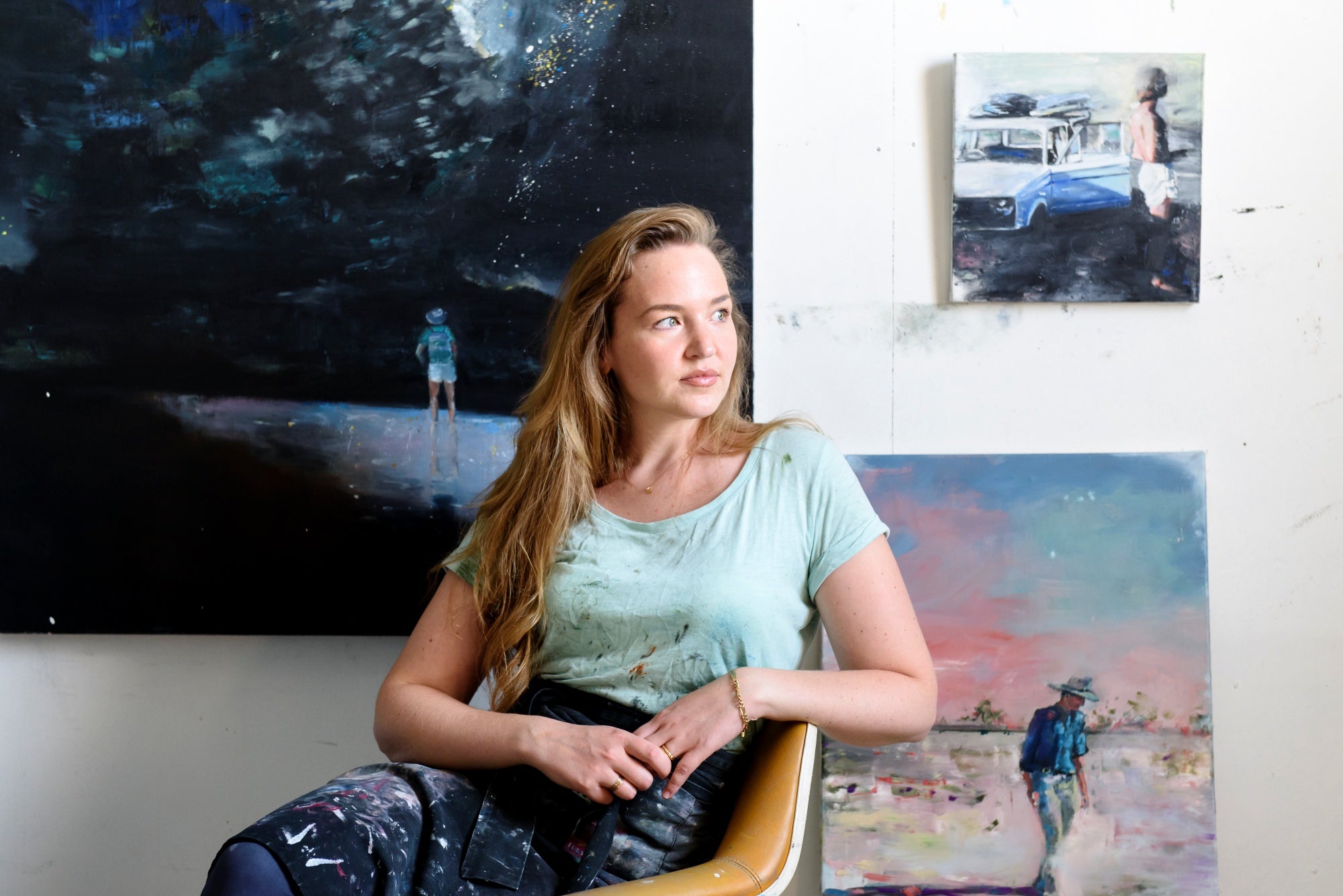 Woman sitting in a chair with paintings on the wall behind her